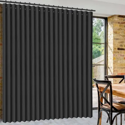 A dark gray pleated curtain hangs in front of a large window with a brick wall visible to the right. A wooden table and chairs are partially visible in the foreground.