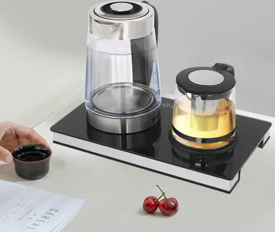 A tea set with a kettle and teapot on a heating base, with a hand holding a tea cup.