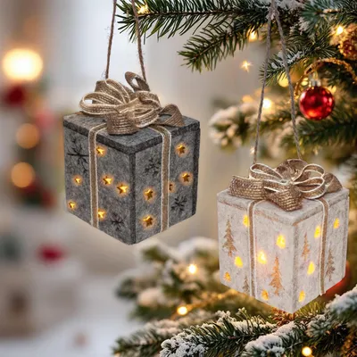 Two illuminated gift box ornaments hanging from a Christmas tree branch.