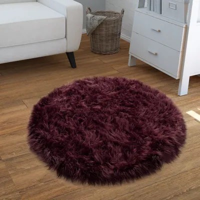 A round, fluffy, violet rug is placed on a wooden floor next to a white sofa and a white dresser. A wicker basket is also visible.