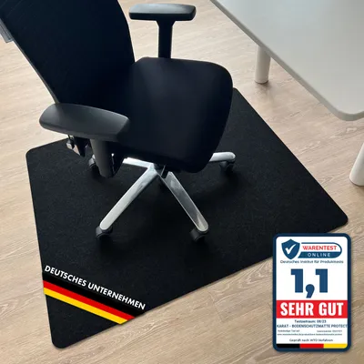 A black office chair is placed on a black floor mat in front of a white desk.
