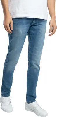 A person wearing blue jeans and white sneakers, shown from the waist down against a white background.