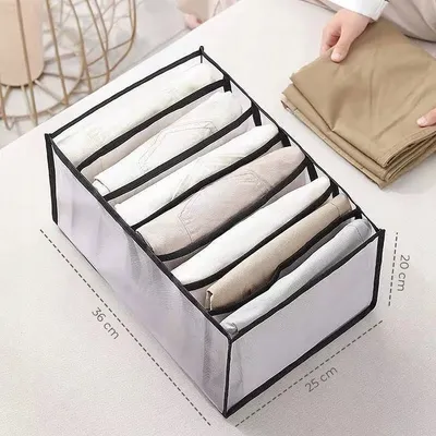 A clothing organizer box filled with folded clothes, with a person's hands holding folded clothes in the background.