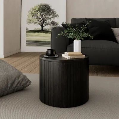 A dark wooden round coffee table with books and a cup on it, placed next to a sofa and a large framed picture of a tree.