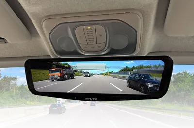 View of a digital rearview mirror inside a vehicle, showing a highway scene with trucks and cars.