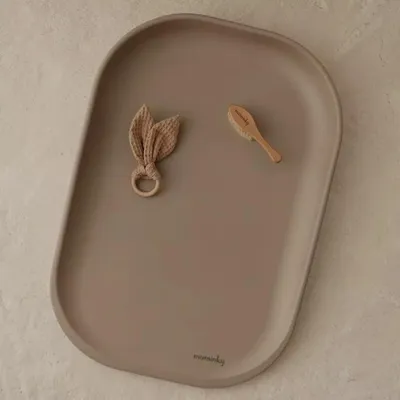 A taupe changing mat with a baby brush and a bunny ear teether on it.