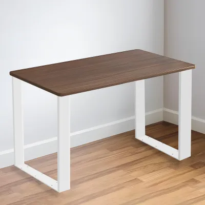 A simple desk with a brown wooden top and white metal legs, placed against a white wall and on a wooden floor.