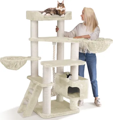 A woman is standing next to a large cat tree with a cat on top.