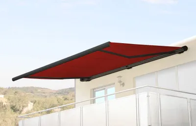 A red retractable awning is extended from a building wall over a balcony.