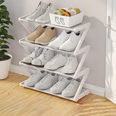 A white zig-zag shoe rack filled with various white and tan shoes, placed next to a doorway on a wooden floor.
