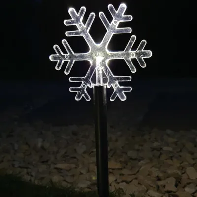 A lit snowflake garden stake at night, with a dark background and gravel in the foreground.