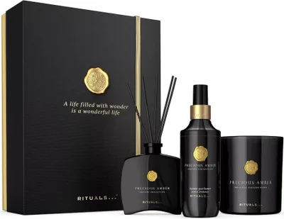 A gift set of Rituals Precious Amber products, including a diffuser, body perfume, and candle, presented in a black gift box.