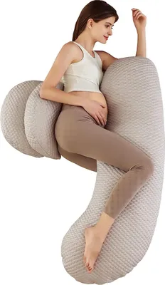 A pregnant woman is lying on her side, using a large, C-shaped pillow for support.