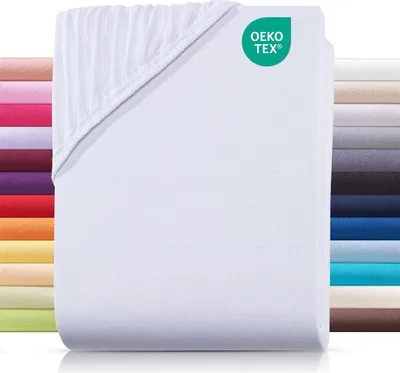 A stack of white jersey fitted sheets with a colorful stack of sheets in the background.