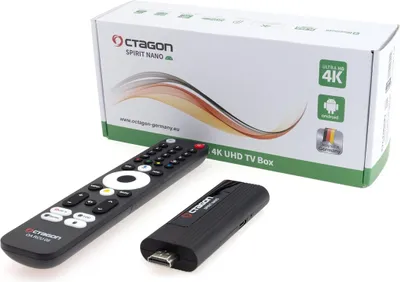 A product shot of a TV box and its accessories, including a remote control and a USB stick, with the product packaging in the background.