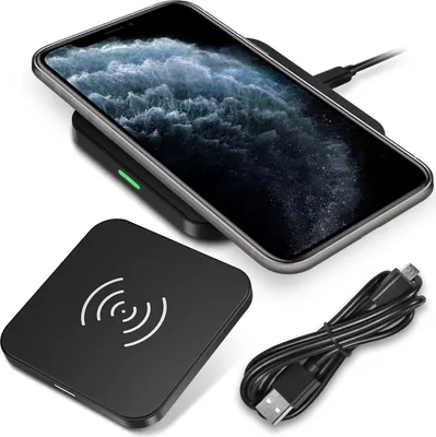 A black wireless charger with a phone on top and a USB cable next to it.