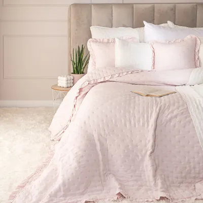 A bed with pink bedding and pillows, a small plant on a side table, and a fluffy rug.
