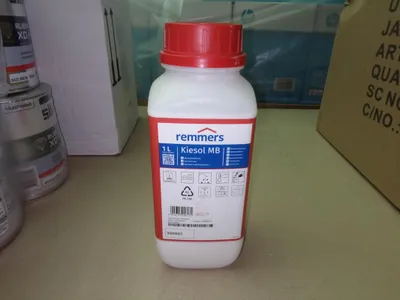 A bottle of Remmers Kiesol MB Spezialgrundierung is placed on a table, with other products and boxes in the background.