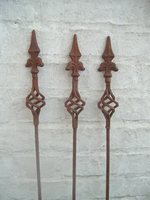 Three metal garden stakes with decorative tops and twisted shafts stand against a white brick wall.