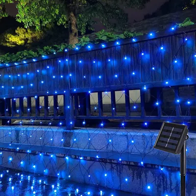 Blue LED net lights are draped over a wooden fence and a stone wall, with a solar panel visible on the right.