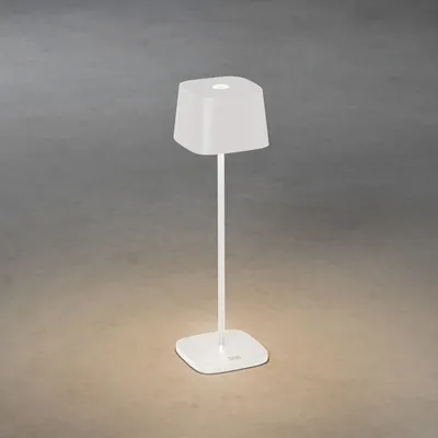 A white table lamp with a square base and a square lampshade is shown against a textured gray and tan background.