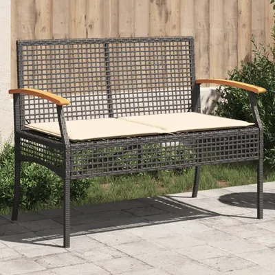 A garden bench with cushions is placed on a patio next to some greenery and a wooden fence.