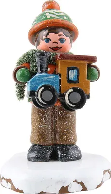 A small, decorative figurine of a child holding a toy train, standing on a snowy base.