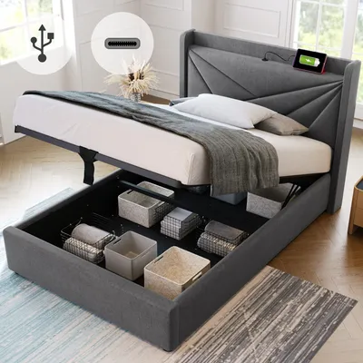 A grey upholstered bed frame with the mattress lifted to reveal storage compartments underneath. A tablet is charging on the headboard.