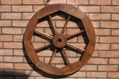 A wooden wagon wheel is mounted on a brick wall.