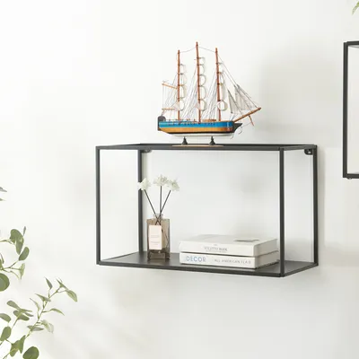 A black metal wall shelf mounted on a white wall, displaying a model ship, a vase with flowers, and two books.