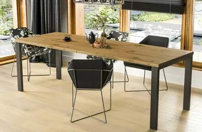 A dining table and chairs set in a modern dining room with large windows overlooking a garden.