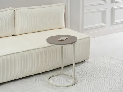 A small round side table with a phone on top, placed next to a cream-colored sofa.
