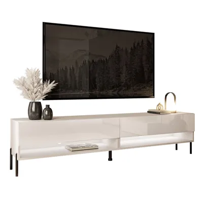 A modern white TV stand with black legs, featuring a large flat-screen TV mounted above it. Decorative items like a vase with dried flowers and a small lamp are placed on the stand.