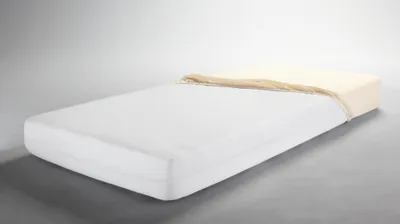 A white mattress with a cream-colored sheet partially covering the top, set against a light gray background.