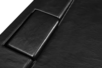 A close-up view of a black shower tray with a textured surface and a raised rectangular section.