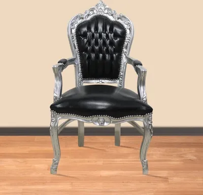 A baroque-style armchair with black faux leather upholstery and a silver-painted frame, set against a plain background with a wooden floor.