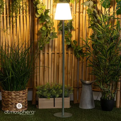 A floor lamp is placed in a garden setting with bamboo fencing and lush greenery.