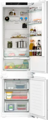An open built-in refrigerator and freezer combination, showing the interior shelves and drawers stocked with food items.