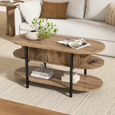 A three-tiered oval coffee table with a wood-grain finish and black metal legs, placed on a rug in a living room setting next to a sofa.