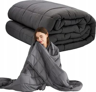 A woman is wrapped in a weighted blanket, with a folded weighted blanket in the background.