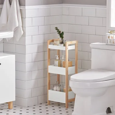 A corner of a bathroom with white subway tiles, a toilet, a storage shelf, and a cabinet.