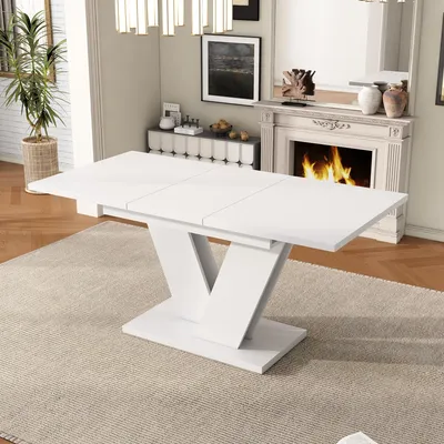 A white dining table with a V-shaped base is shown in a well-lit room with a fireplace in the background.