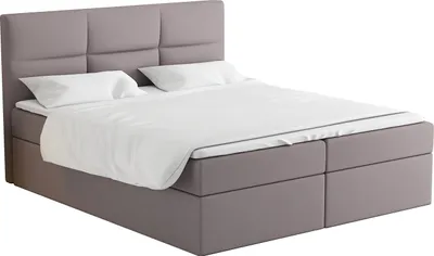 A studio shot of a beige box spring bed with white bedding.