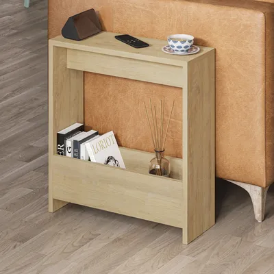 A light wood side table with books, a remote, a speaker, and a cup of tea next to a brown leather sofa.