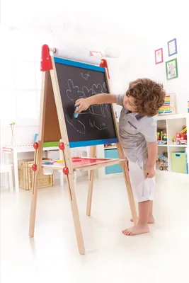 A young boy is drawing on a blackboard easel in a brightly lit room.