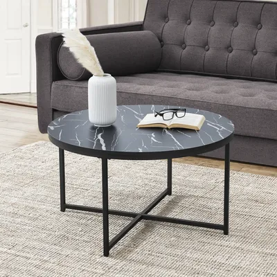 A round coffee table with a marble-patterned top and black metal legs is placed on a rug in front of a gray sofa.