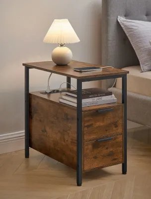 A bedside table with a lamp, books, and a phone, placed next to a bed.