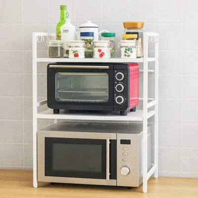 A white shelving unit with two microwaves and various kitchen containers on the top shelf, set against a tiled wall.