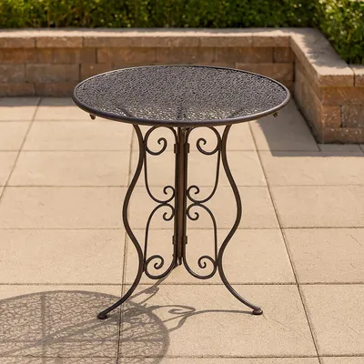 A round metal garden table with an ornate base is shown on a paved patio.