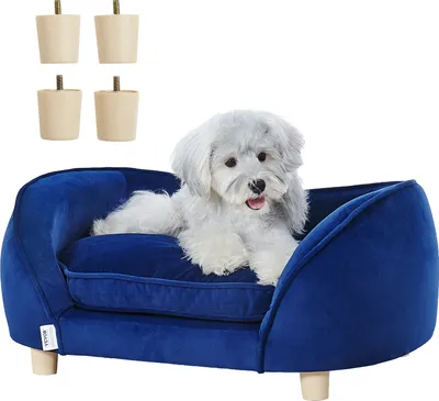 A small, fluffy white dog is lying on a dark blue pet sofa. Four beige legs for the sofa are shown in the top left corner.